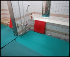 入浴訓練の風景画像1　洗い場全体に床面にマットを敷き詰めて、いざりながらシャワー近くに行けるようにしている様子