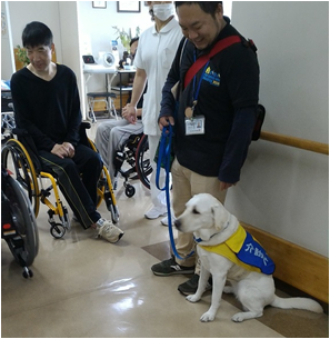 車椅子使用者の前に介助犬訓練師が、介助犬をお座りさせている様子