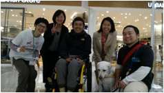 車椅子使用者の横に介助犬が座り、そこを中心に、日本介助犬協会のスタッフ、当センタースタッフが囲み記念写真を撮っている様子
